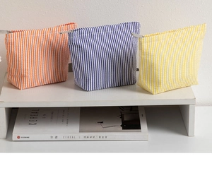 Close-up of three colorful seersucker stripe pouches with metal zipper on a white shelf