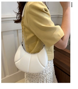 Detail of white pleated crescent bag with gold chain strap worn on the shoulder