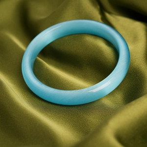 Detail of light blue cat-eye stone bangle with smooth finish on green silk fabric