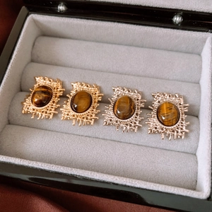 Macro shot of gold and silver oval tiger eye stone earrings on a grey velvet tray