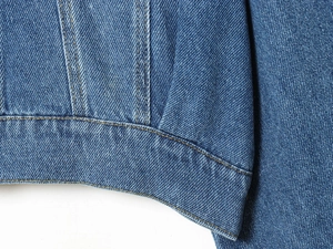 Detailed macro view of denim jacket hem showing precise golden double stitching and fabric