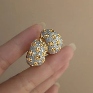 Macro shot of light blue enamel C-shape hoop earrings with vintage gold flower and diamond inlay