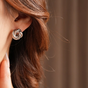 Macro shot of silver twisted knot stud earrings showing metal luster on a model