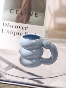 Close-up of blue ceramic mug with unique cloud shape design and thick handle on glass table