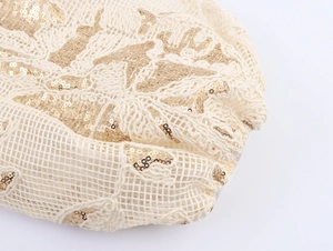 Detailed close-up of cream mesh fabric featuring intricate gold sequin embroidery pattern