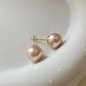 Macro shot of elegant champagne pearl stud earrings with gold needles on white ceramic tray