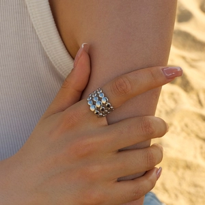 Close-up of a silver multi-layer beaded ring shown on a finger at a golden beach