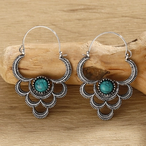 Detailed view of silver bohemian fan earrings with turquoise bead on a wood branch