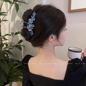 Détail de la pince à cheveux camélia bleu avec strass sur une coiffure élégante relevée
