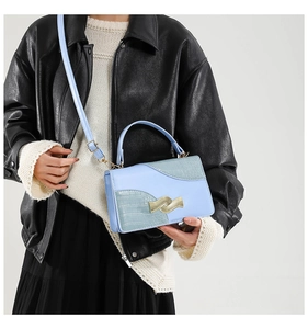 Detail of light blue crossbody bag with crocodile texture and gold wavy buckle