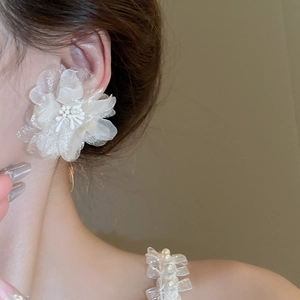 Close-up of white mesh flower earring with delicate petal textures on a model's ear