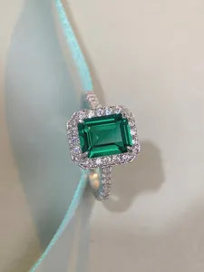 Macro shot of 3ct emerald cut green stone ring with halo setting on blue satin