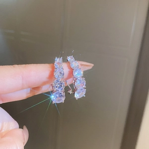 Macro detail of curved silver earrings with four sparkling zircons on finger