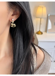 Close-up of a golden rocking horse earring with a white pearl on a model's ear