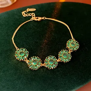 Detailed close-up of a gold-plated bracelet featuring emerald green flower gems on velvet