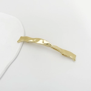 Detail of golden wave-shaped metal hair clip with a polished finish on white background