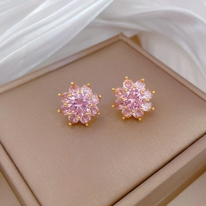 Macro detail of sparkling pink zircon flower earrings on elegant white silk background