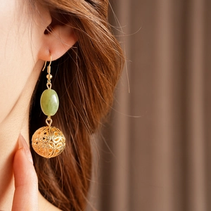 Detail of hollow golden spherical earrings with green oval beads on female model