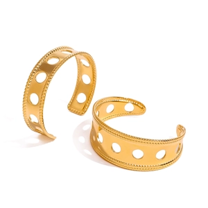Detail of gold wide cuff bracelets featuring round hollow cutouts and rope textured edges