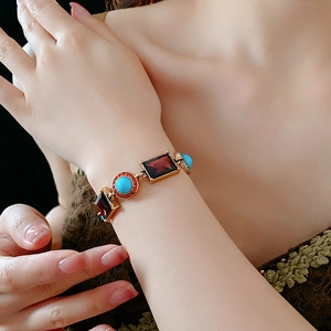 Close-up of vintage golden bracelet with red and turquoise gems on a model's wrist