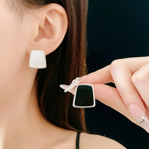 Détail de boucles d'oreilles trapèze en résine nacre blanche et onyx noir sur un modèle