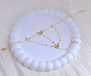 Detailed macro view of gold-plated butterfly bracelet with pearl charms on a white tray