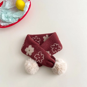 Close-up of a deep red knit children's scarf with beige floral patterns and pom-poms