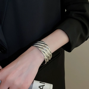 Gros plan d'un bracelet manchette argenté à texture ondulée sur un mannequin