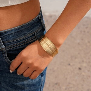 Detail of a wide gold metal multi-layered wrap cuff bracelet on model's wrist