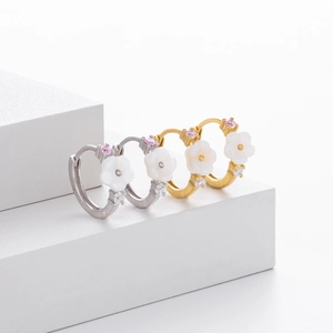 Detailed view of silver and gold flower earrings with mother of pearl on a white pedestal