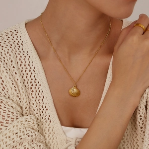 Detail of a delicate gold shell pendant necklace worn on a woman's collarbone