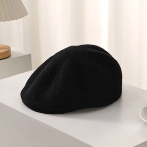 Close-up of black wool beret with metal logo detail on a white display surface