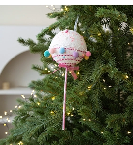 Close-up of pink lollipop Christmas ornament with colorful pom-poms on tree branch