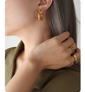 Close-up of model wearing 18K gold-plated C-shape twisted earrings and chunky gold rings