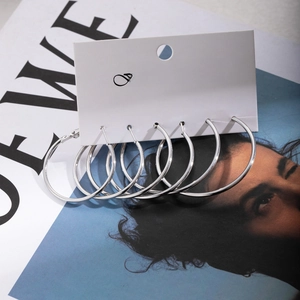 Three pairs of high-polish silver hoop earrings in varying sizes on a minimalist display