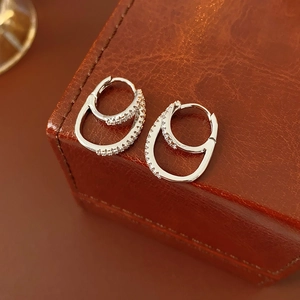 Detail of silver double-hoop earrings with zircon inlay on a brown leather jewelry box
