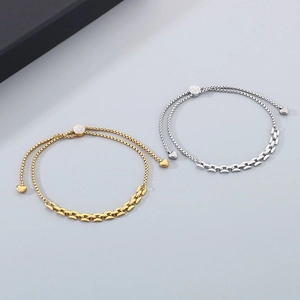 Detail of titanium steel bracelet with H-link design, gold finish and heart charm