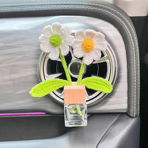 Close-up of a glass car perfume bottle with handmade knitted daisy flowers and wooden lid