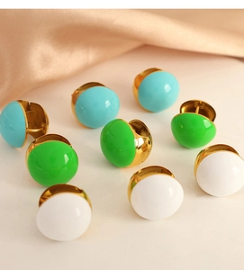 Detailed macro view of gold-plated enamel stud earrings in blue, green, and white
