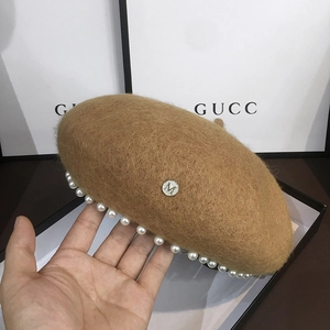 Detailed view of wool beret featuring pearl edges and a round metal M logo badge