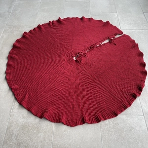 Close-up of a large dark red knitted Christmas tree skirt with textured wave edges and ties