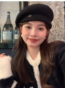 Close-up of a black wool beret featuring a metallic ML logo and soft knit cardigan details