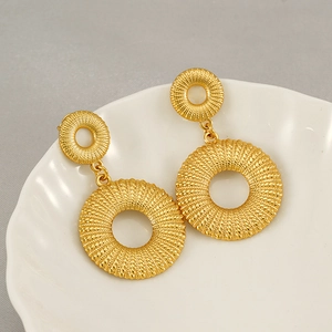 Close-up of gold double-hoop earrings with intricate woven texture on a white ceramic plate