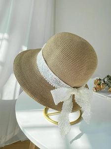 Detailed view of straw sun hat with white lace ribbon bow on elegant gold display stand
