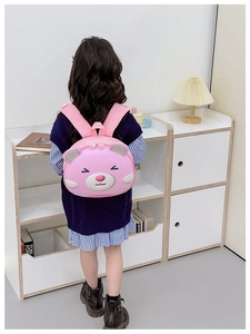 Pink cartoon bear hardshell backpack for toddlers shown on a girl in a cozy home setting