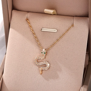 Elegant gold snake necklace with sparkling white crystals and green stone eyes in a gift box