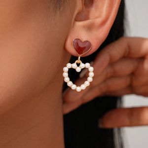 Close-up of elegant red enamel heart and faux pearl drop earrings on a female model