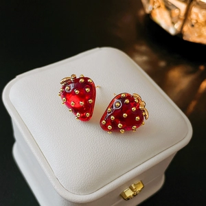 Close-up of red strawberry stud earrings with glossy finish on white jewelry box