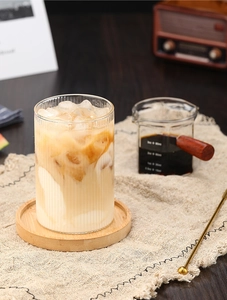 Primer plano de un vaso acanalado de borosilicato con café helado en posavasos de madera