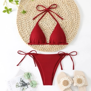 Detailed flat lay of a burgundy ribbed halter bikini set on a woven mat with summer decor